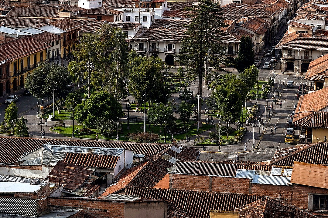Elevated panoramic view of a dense Andean city centered on a leafy public plaza and surrounded by mountains.
