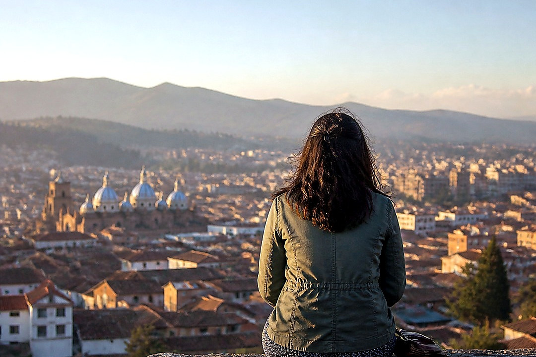 A solitary woman overlooks the San Francisco skyline from a stone wall.